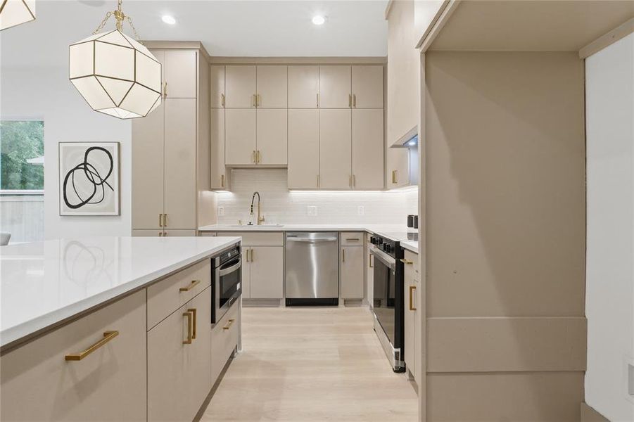 Contemporary kitchen featuring an expansive island with a built-in microwave, light-toned cabinetry with gold-finish hardware, stainless steel appliances, and wood-finish flooring Contemporary kitchen featuring an expansive island with a built-in microwave, light-toned cabinetry with gold-finish hardware, stainless steel appliances, and wood-finish flooring