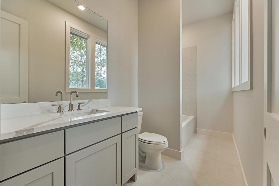 Stylish secondary en-suite bath featuring quartz countertops, soft grey cabinetry, and a clean tub-shower combo for everyday comfort.