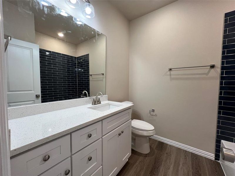 Hall Bathroom with hardwood / wood-style floors, vanity, toilet, and tiled shower