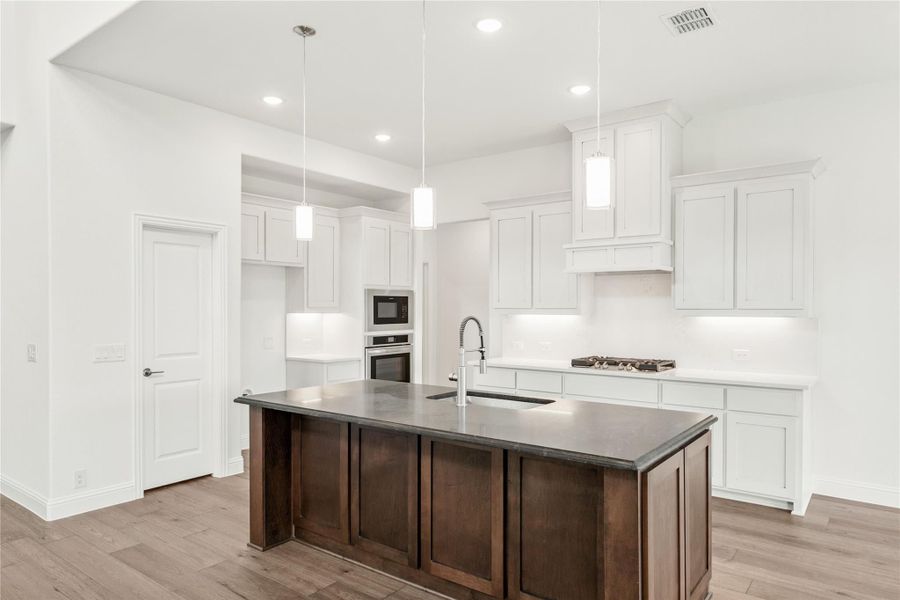 Kitchen with white cabinets, dark wood island, pendant lights, and stainless steel appliances on hardwood floors