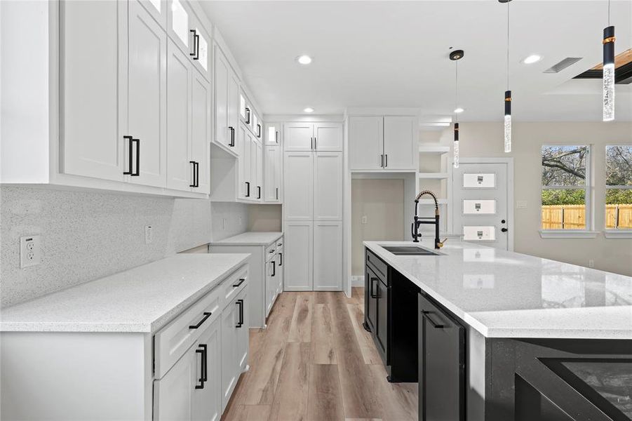 Kitchen featuring light stone countertops, tasteful backsplash, sink, decorative light fixtures, and white cabinetry