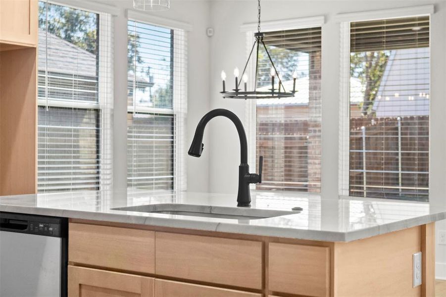 Kitchen featuring light brown cabinetry, hanging light fixtures, stainless steel dishwasher, and light stone counters