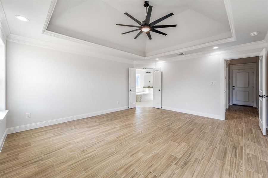 Empty room featuring ceiling fan, a tray ceiling, ornamental molding, and light wood-type flooring