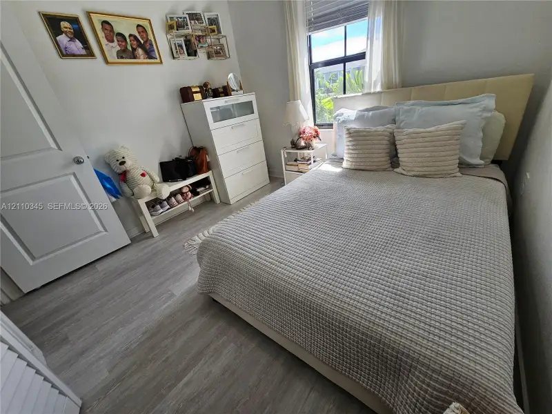 Bedroom featuring wood-finish flooring, a single-panel interior door, and a multi-pane window