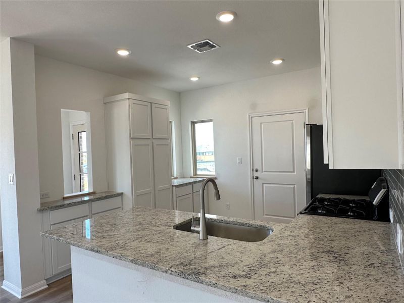 Kitchen featuring a peninsula, light stone counters, recessed lighting, black gas range, and white cabinets