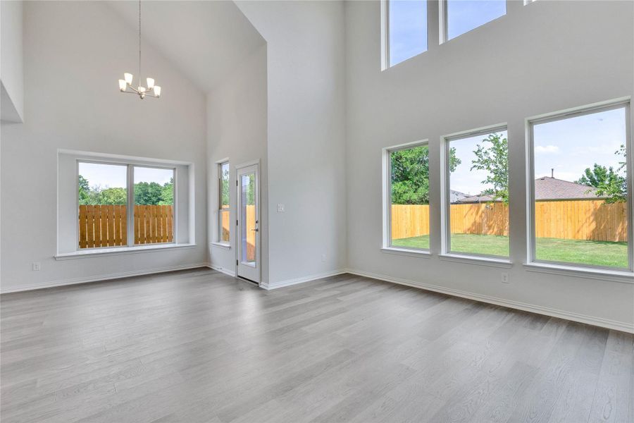 Unfurnished living room with high vaulted ceiling, plenty of natural light, a chandelier, wood finished floors, and baseboards Unfurnished living room with high vaulted ceiling, plenty of natural light, a chandelier, wood finished floors, and baseboards