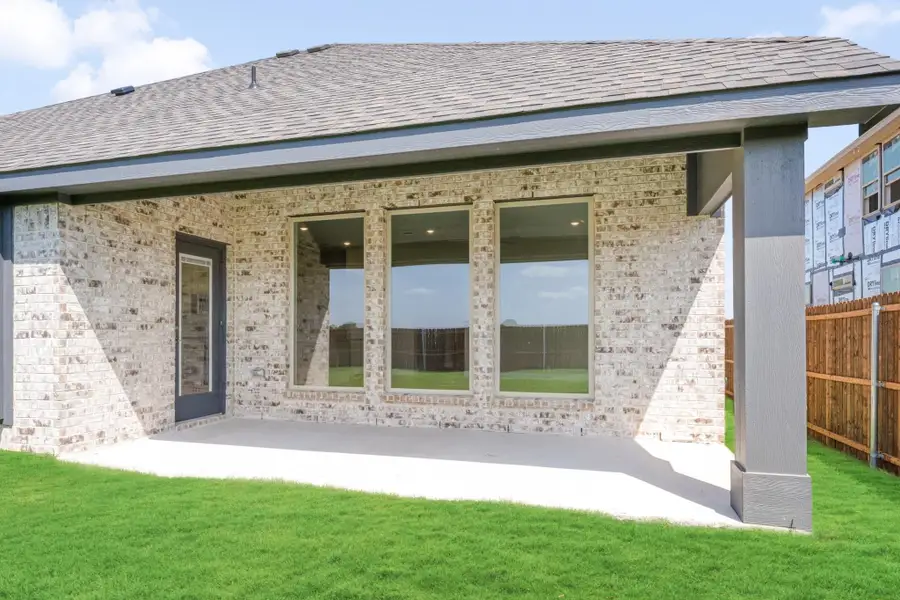Rear exterior of brick home with covered patio, large windows, and green backyard lawn