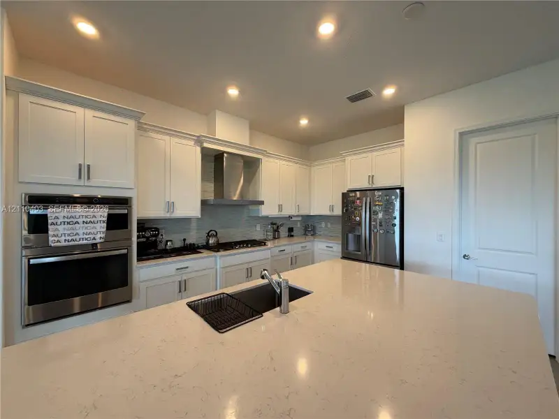 Kitchen featuring white cabinetry, an expansive central island with a quartz countertop, stainless steel appliances including a built-in wall oven, and recessed lighting