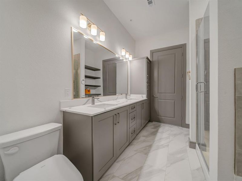 Bathroom featuring double vanity, light marble finish flooring, and a stall shower