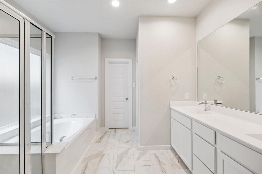 This primary bathroom features a modern design with a spacious layout. It includes a large mirror above a dual-sink vanity, a separate bathtub, and a shower with glass doors. The space is bright and finished with sleek, white cabinetry and marble-style flooring. This primary bathroom features a modern design with a spacious layout. It includes a large mirror above a dual-sink vanity, a separate bathtub, and a shower with glass doors. The space is bright and finished with sleek, white cabinetry and marble-style flooring.