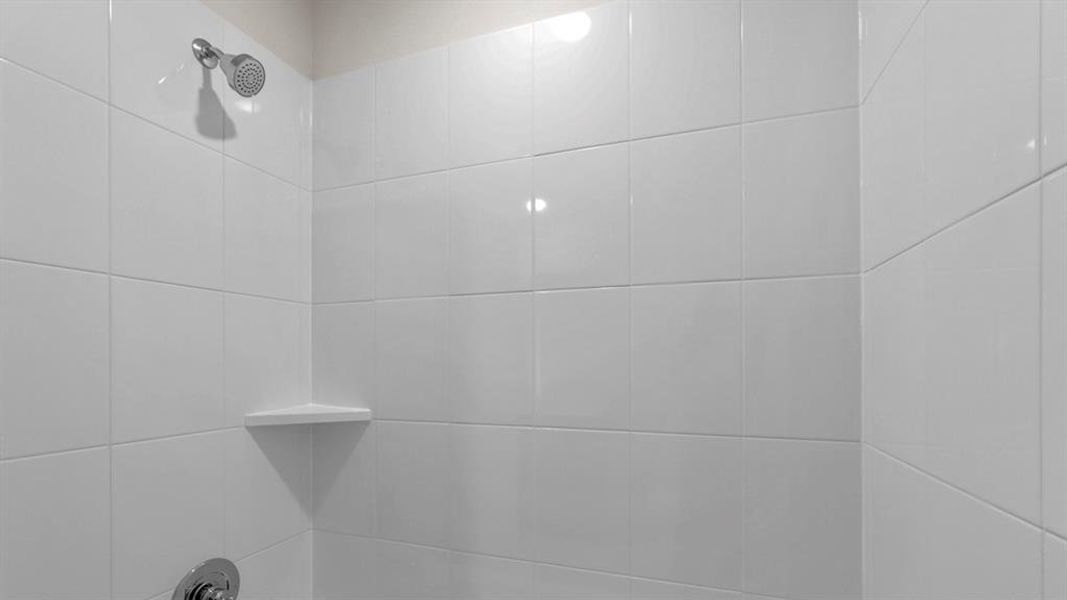 White tiled shower with a chrome showerhead and a built-in corner shelf