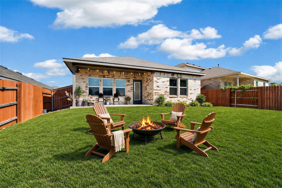 Virtually staged - View of backyard featuring a verdant lawn provides a serene setting for a backyard fire pit, framed by a welcoming patio and brick home.
