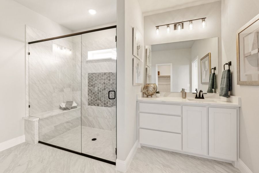 Bathroom with glass walk-in shower, marble tile walls, white vanity, and large mirror with overhead lighting