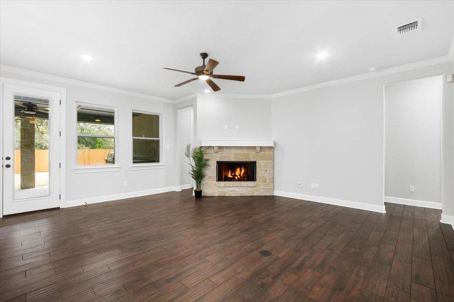 Unfurnished living room featuring ceiling fan, dark wood-type flooring, ornamental molding, a stone fireplace, and baseboards Unfurnished living room featuring ceiling fan, dark wood-type flooring, ornamental molding, a stone fireplace, and baseboards