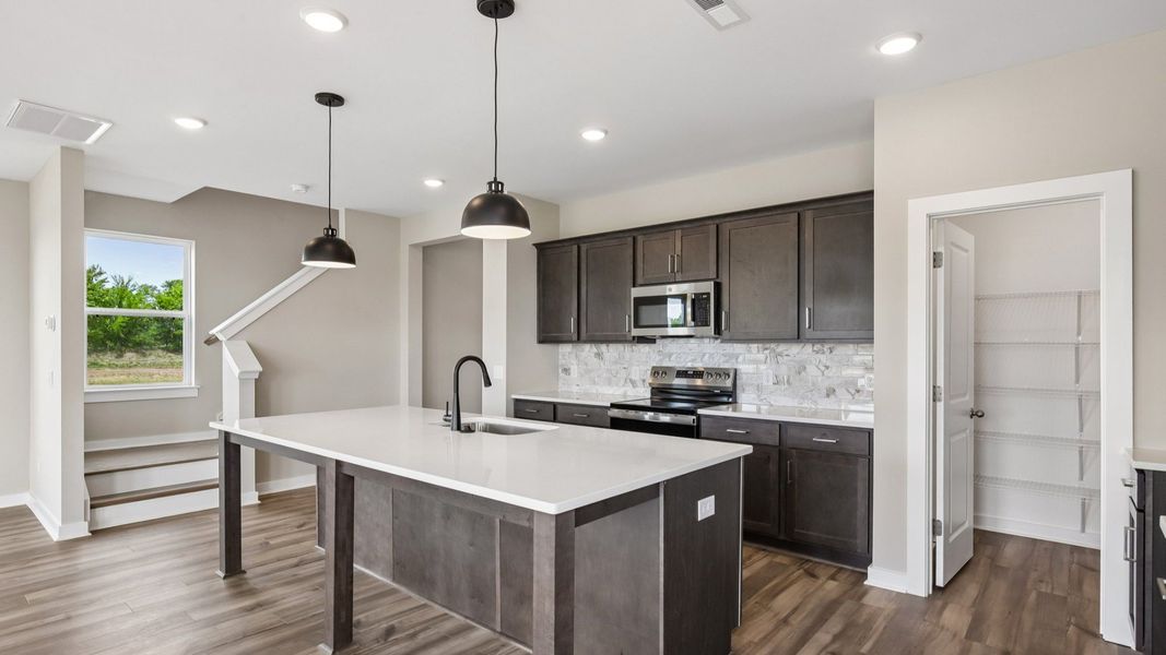 Kitchen with dark cabinetry, quartz countertops, and tile backsplash and pantry Kitchen with dark cabinetry, quartz countertops, and tile backsplash and pantry