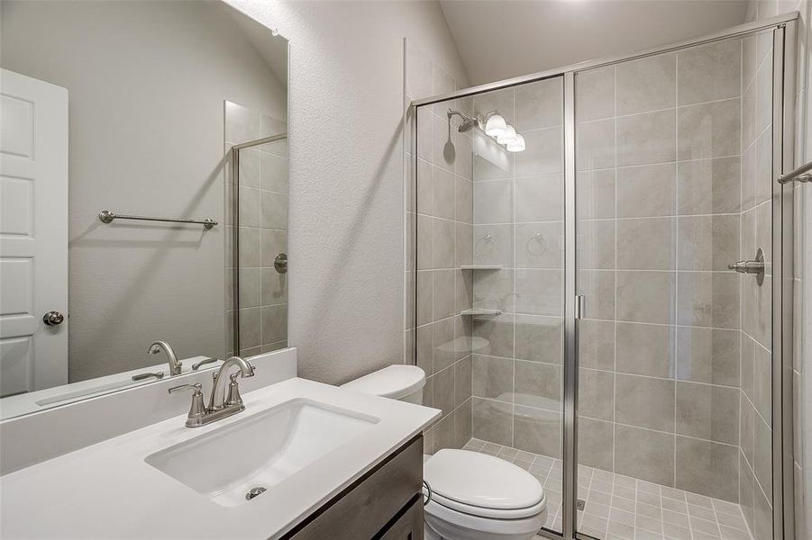 Bathroom with a shower with shower door, vaulted ceiling, vanity, and toilet Bathroom with a shower with shower door, vaulted ceiling, vanity, and toilet