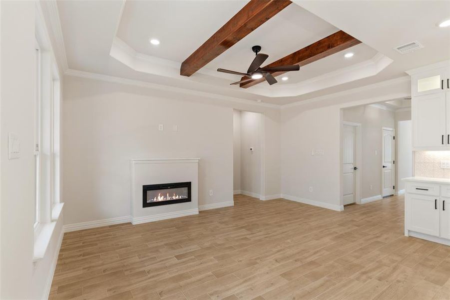 Unfurnished living room with ceiling fan, ornamental molding, beamed ceiling, and light wood-type flooring