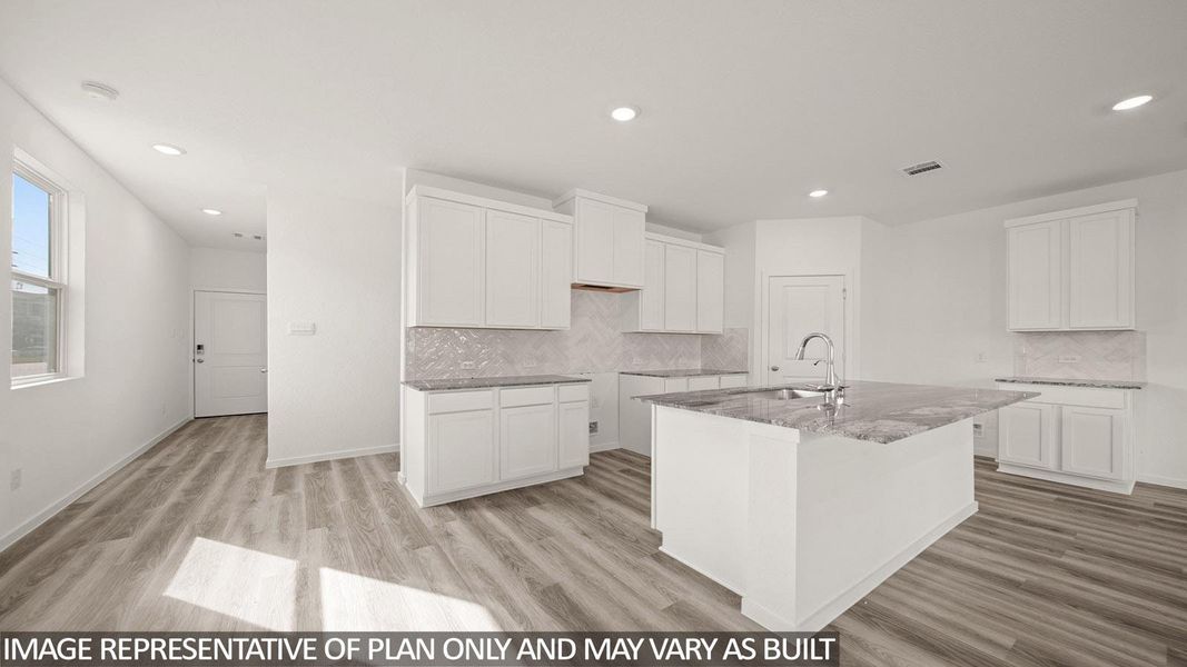 Kitchen featuring a central island with an integrated sink, white cabinetry, light-toned countertops, a light-toned backsplash, and recessed lighting