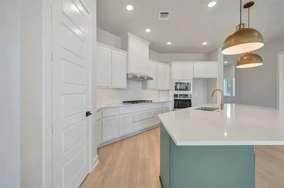 Dual tone kitchen featuring a center island with sink, light wood-style flooring, stainless steel appliances, hanging light fixtures, and two tone cabinets Dual tone kitchen featuring a center island with sink, light wood-style flooring, stainless steel appliances, hanging light fixtures, and two tone cabinets