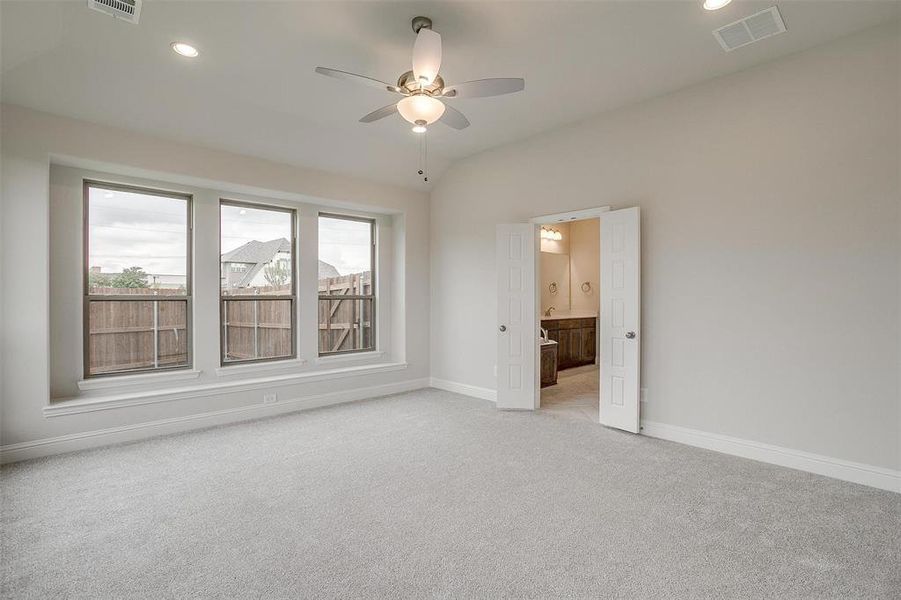 Unfurnished bedroom featuring ceiling fan, light carpet, multiple windows, and connected bathroom