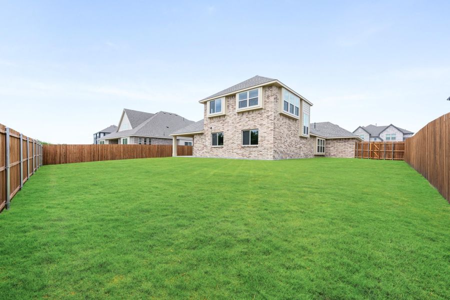 Two-story brick home with large grassy backyard enclosed by wood privacy fence Two-story brick home with large grassy backyard enclosed by wood privacy fence