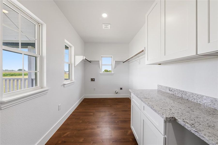 Bright utility space featuring wood-finish flooring, white cabinetry, and a speckled countertop