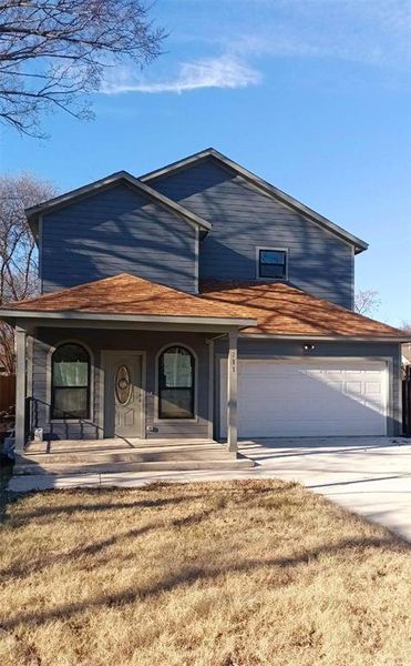 View of front of property with a front yard, covered porch, and a garage