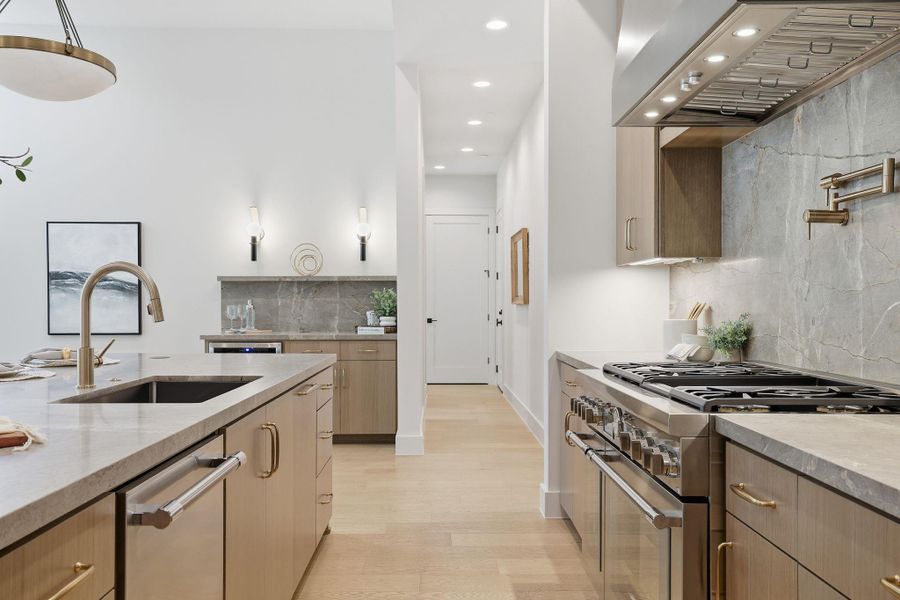 Kitchen with stainless steel appliances, light stone countertops, premium range hood, light brown cabinetry, and tasteful backsplash
