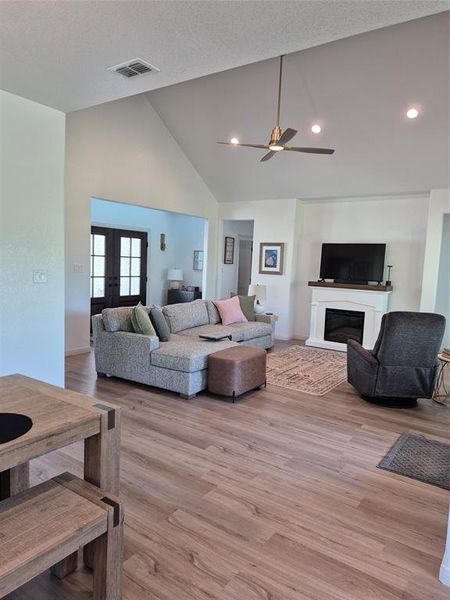 Living room featuring a glass covered fireplace, high vaulted ceiling, french doors, light wood-style flooring, and ceiling fan