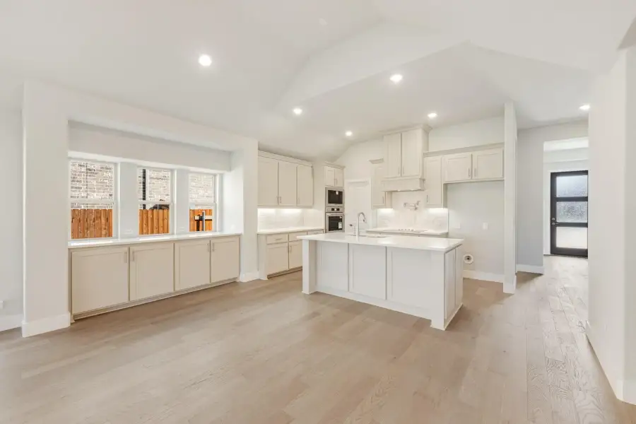 Open kitchen with white cabinets, center island, and light hardwood floors under vaulted ceiling