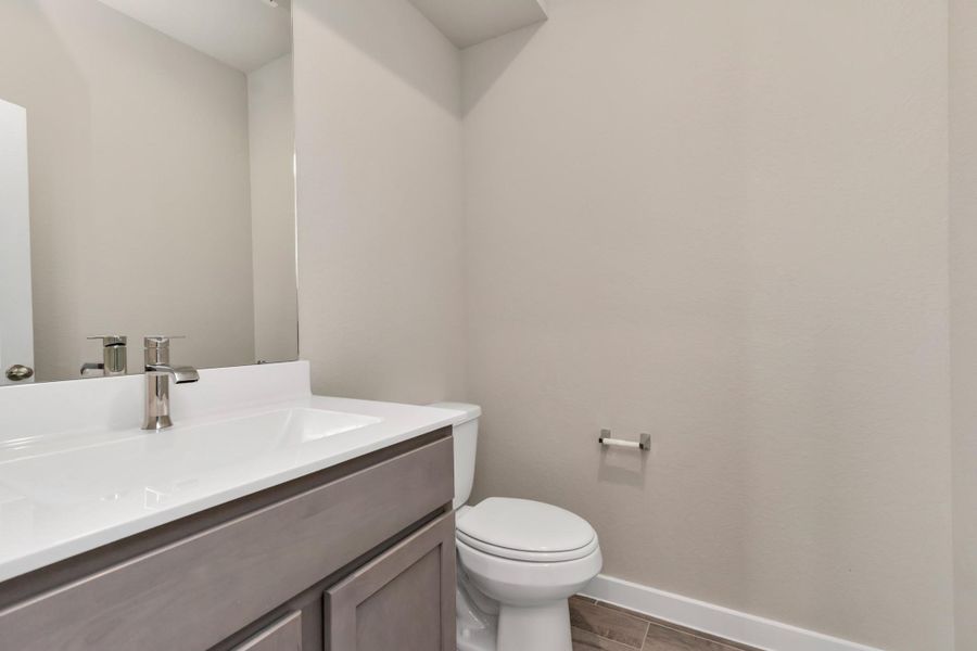 The half bathroom, conveniently situated on the 1st floor, is adorned with contemporary finishes. Slate  cabinets paired with a light countertop, custom wall paint, and a sleek faucet combine to create a bright and inviting space. Sample photo of completed home with similar floor plan. As-built interior colors and selections may vary.