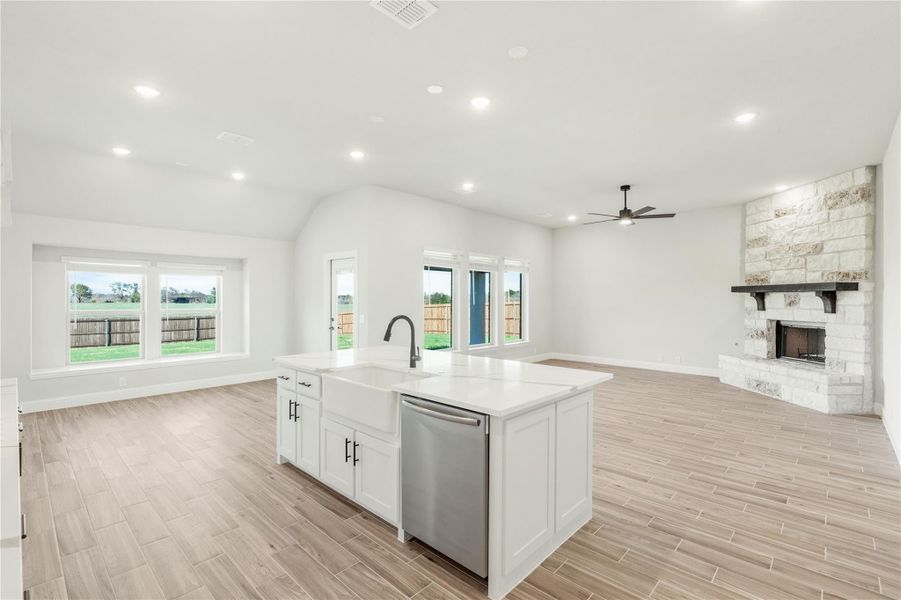 Open-concept kitchen and living area with white island, stone fireplace, and wood-look tile floors Open-concept kitchen and living area with white island, stone fireplace, and wood-look tile floors