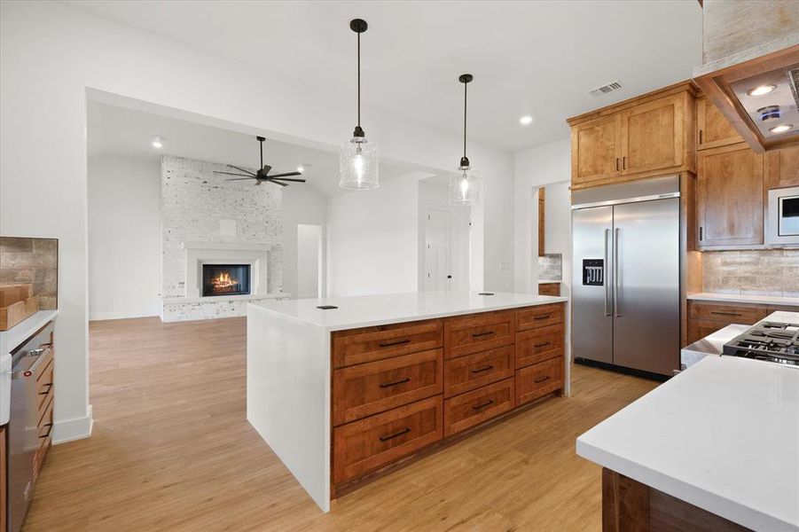 Kitchen with brown cabinetry, a kitchen island, pendant lighting, a fireplace, and built in appliances
