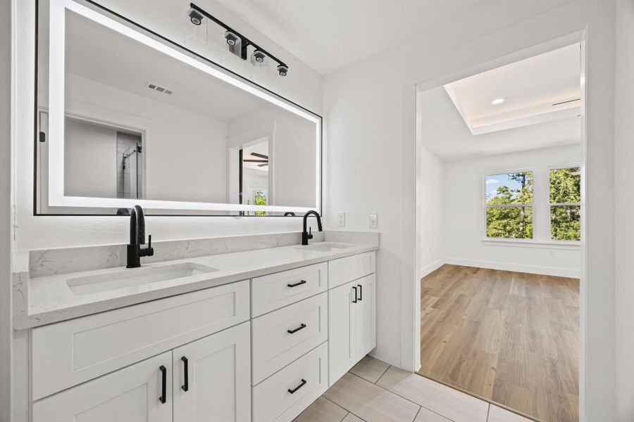 Full bath featuring double vanity, a shower stall, and light wood finished floors