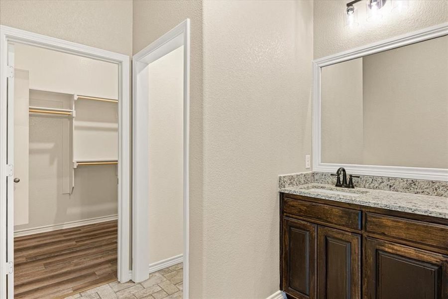 Bathroom with a textured wall, a walk in closet, and vanity