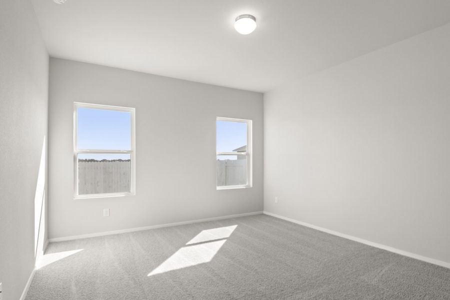 Image of a primary bedroom with light grey walls, tan carpeting, two windows and white trim