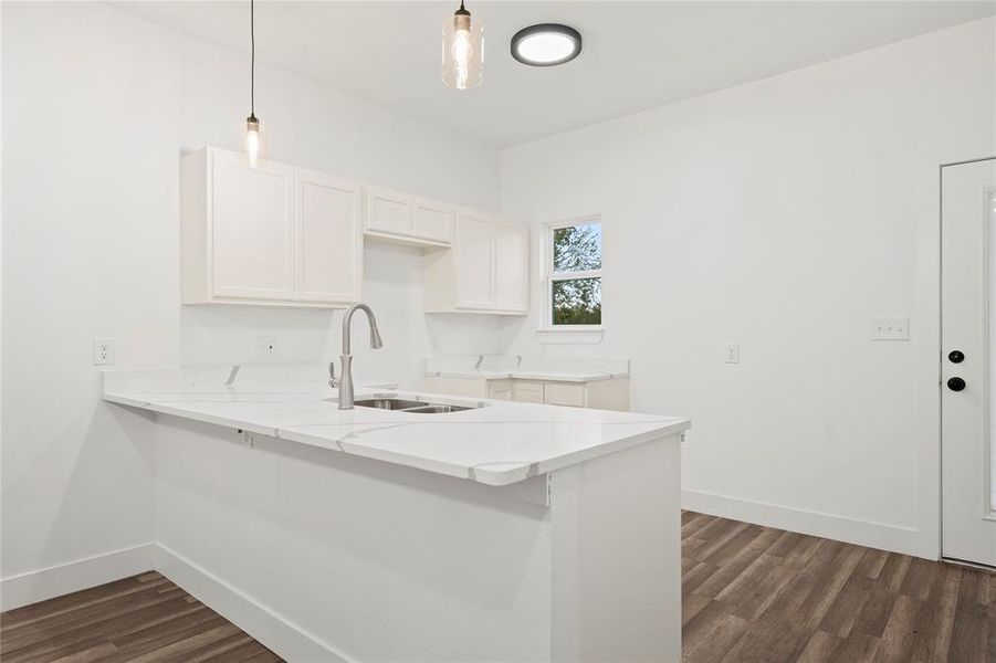 Kitchen featuring kitchen peninsula, dark hardwood / wood-style flooring, sink, white cabinetry, and hanging light fixtures