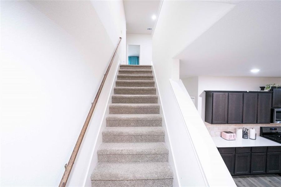 Carpeted staircase with a wood-finish handrail, leading to an upper level Carpeted staircase with a wood-finish handrail, leading to an upper level