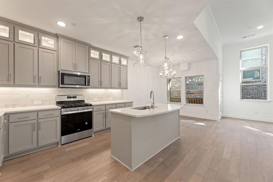 Kitchen featuring hanging light fixtures, a center island with sink, sink, light hardwood / wood-style floors, and stainless steel appliances