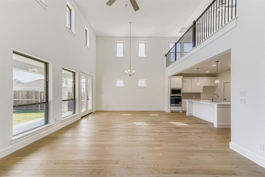 Unfurnished living room with light wood-type flooring, a towering ceiling, ceiling fan, and a chandelier Unfurnished living room with light wood-type flooring, a towering ceiling, ceiling fan, and a chandelier