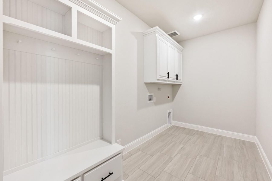 Laundry and mudroom combo with white built-in cubbies, upper cabinets, washer hookups, and light wood-look tile floors
