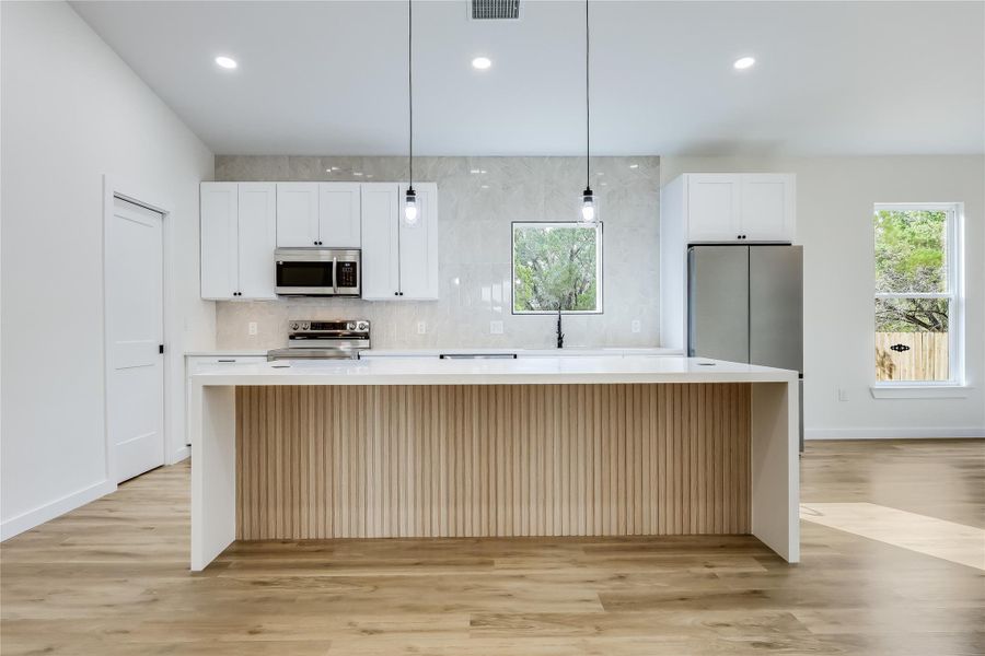 Kitchen featuring appliances with stainless steel finishes, a center island, light wood-style flooring, light countertops, and recessed lighting Kitchen featuring appliances with stainless steel finishes, a center island, light wood-style flooring, light countertops, and recessed lighting