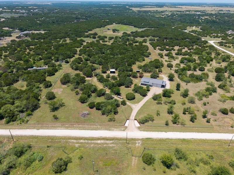 Aerial View of property, entrance, full fencing with 2 pastures to rotate livestock, chip n seal driveway, and custom barndo.