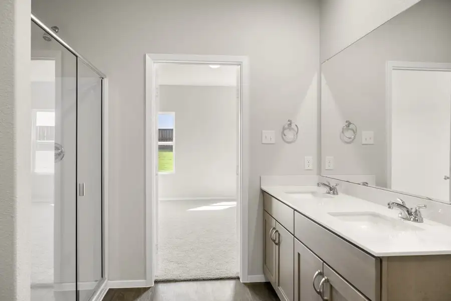 Image of home primary bathroom with vanity with white countertop and light brown cabinets and mirror, and doorway to bedroom with walk-in shower