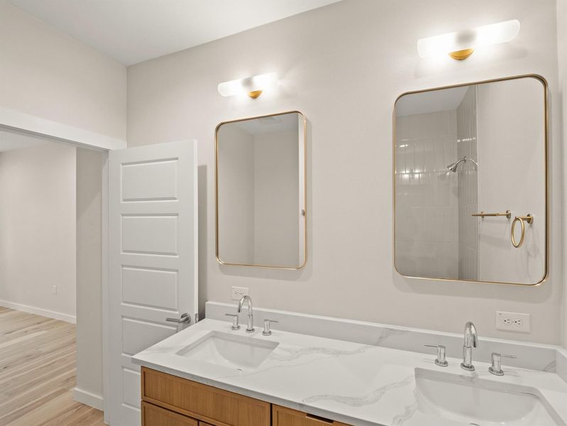 Double vanity featuring white countertops with integrated sinks, wood-finish cabinetry, and gold-framed mirrors