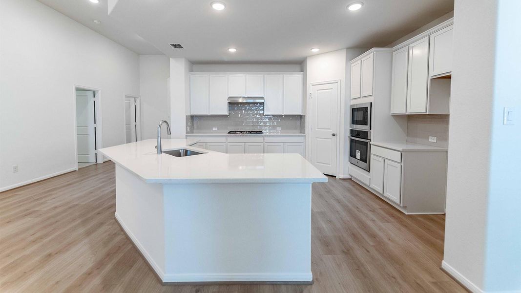Kitchen featuring backsplash, an island with sink, white cabinetry, light wood-style floors, and recessed lighting