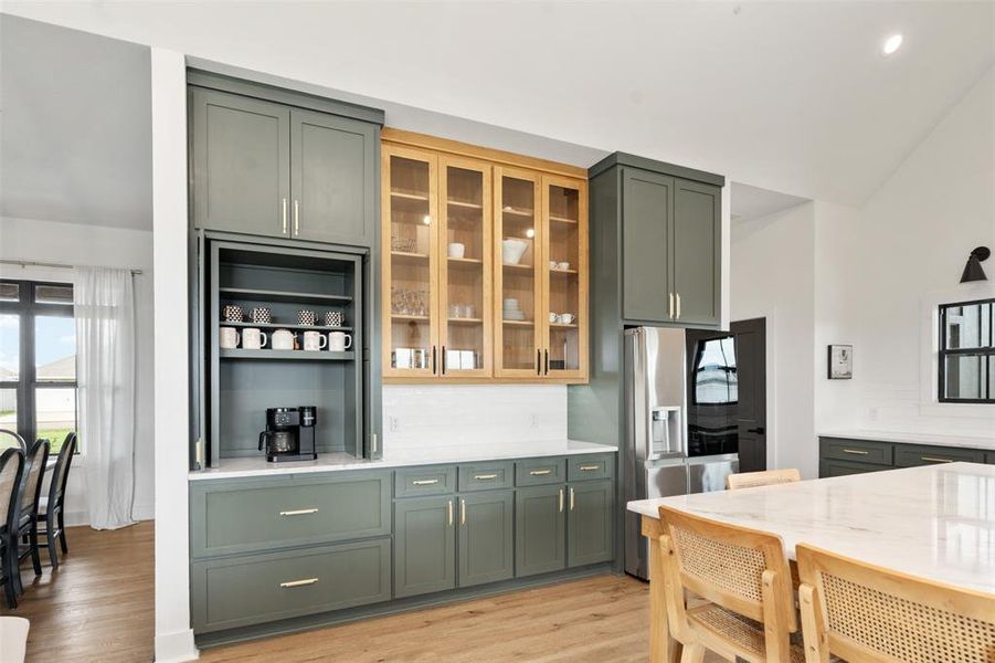 Kitchen featuring stainless steel fridge with ice dispenser, tasteful backsplash, light wood finished floors, glass insert cabinets, and green cabinetry