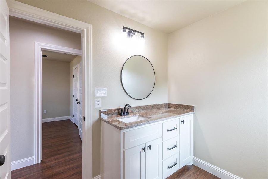 Bathroom vanity featuring a granite countertop with an integrated sink, white cabinetry with dark hardware, and a round wall-mounted mirror