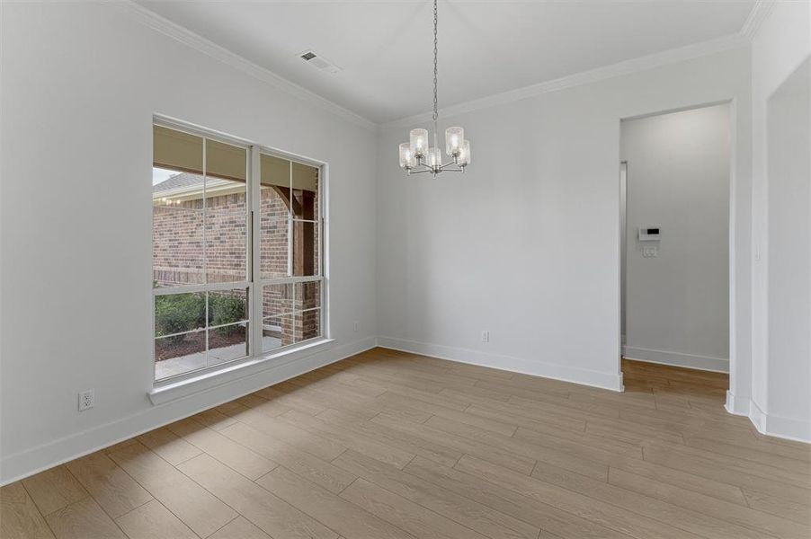Spacious room featuring wood-finish flooring, white walls, and a modern chandelier Spacious room featuring wood-finish flooring, white walls, and a modern chandelier