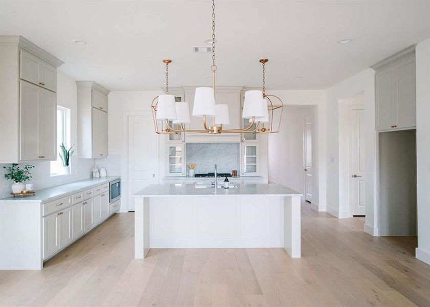 Kitchen featuring stainless steel microwave, backsplash, a center island with sink, hanging light fixtures, and a notable chandelier